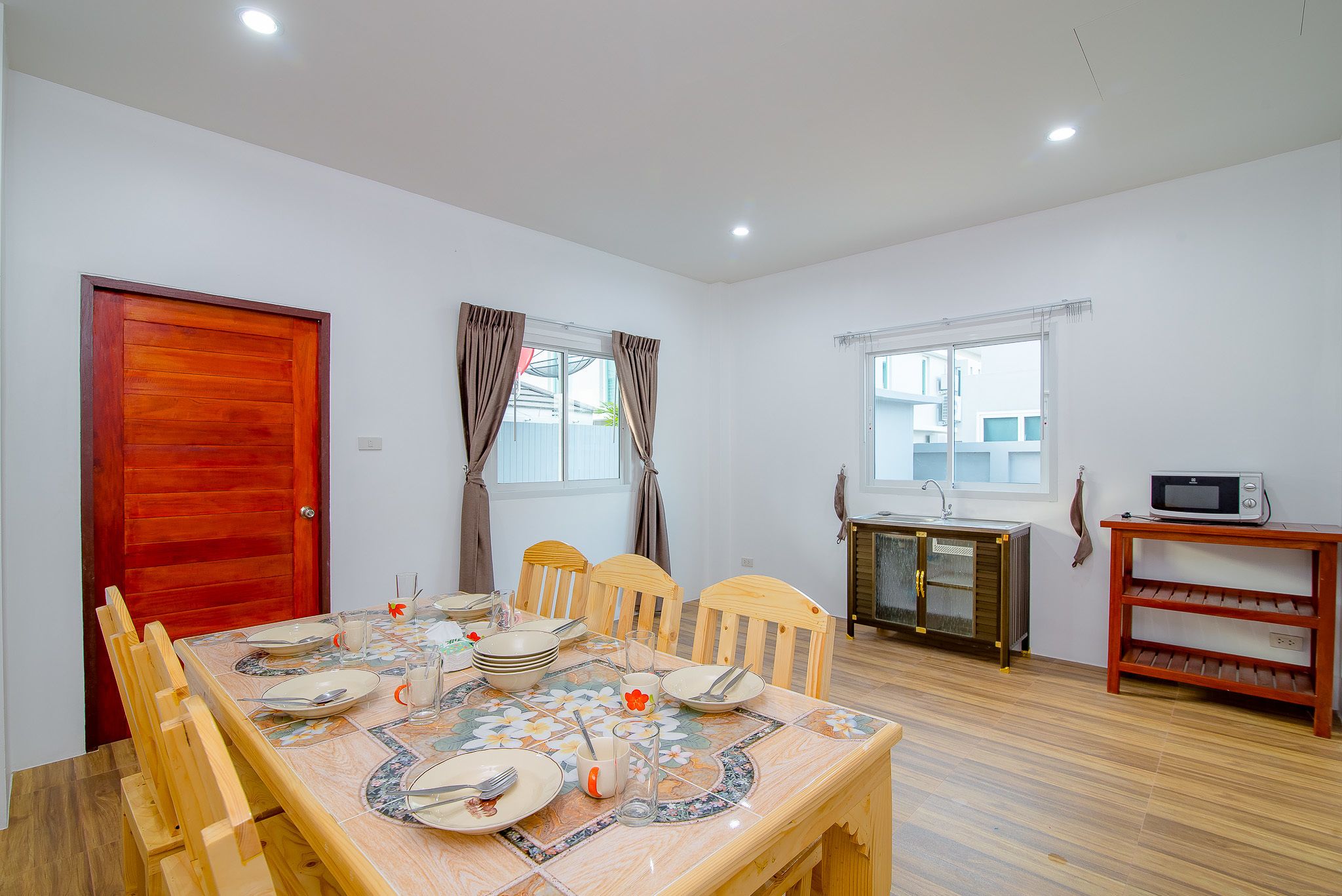 A dining area with a wooden table set for four, a red door, and a kitchenette with a microwave.