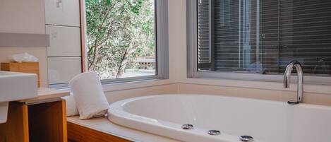 Un baño moderno con una bañera grande, tocador de madera y una ventana con persianas.