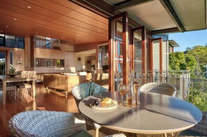 A modern outdoor dining area with wicker furniture, a round table, and a view of the surrounding landscape. - Noosa Residences (Noosa Heads)