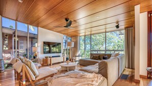 A spacious living room with a wooden ceiling, large windows, a flat-screen TV, and a comfortable seating area.