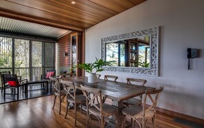 A dining area with a wooden table and chairs, a potted plant, and a decorative mirror on the wall. - Noosa Residences (Noosa Heads)