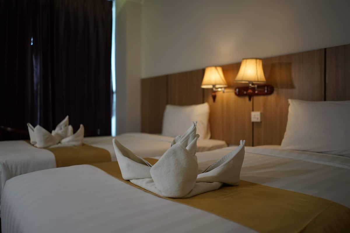 A hotel room with two beds, each with a white bedspread and a decorative towel arrangement. There are two wall-mounted lamps on the headboard.