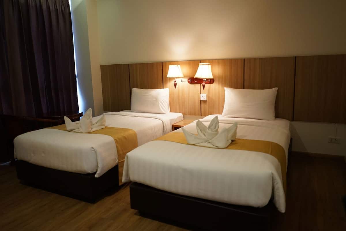A hotel room with two beds, wooden headboard, bedside lamps, and a window with curtains.