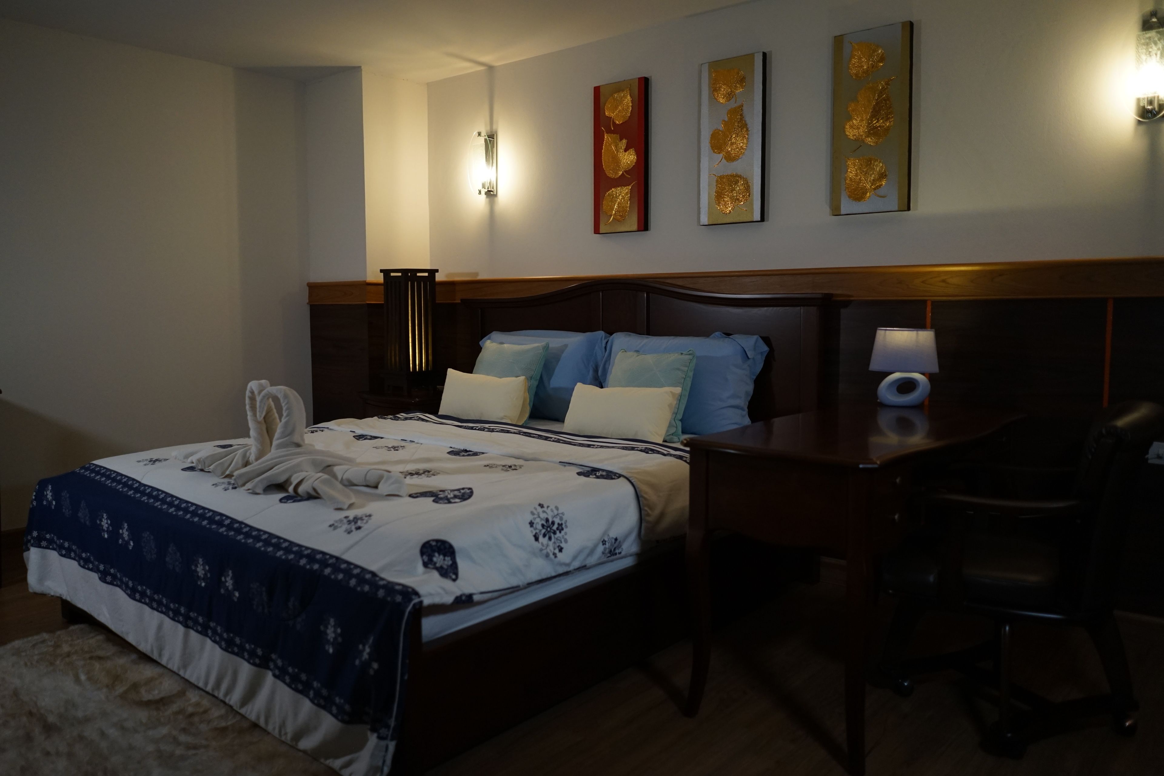 A hotel room with a bed, bedside table, lamp, and wall art.
