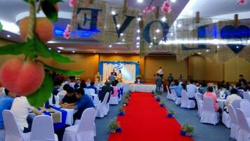 A banquet hall with round tables and chairs, a red carpet, and a stage with a backdrop.