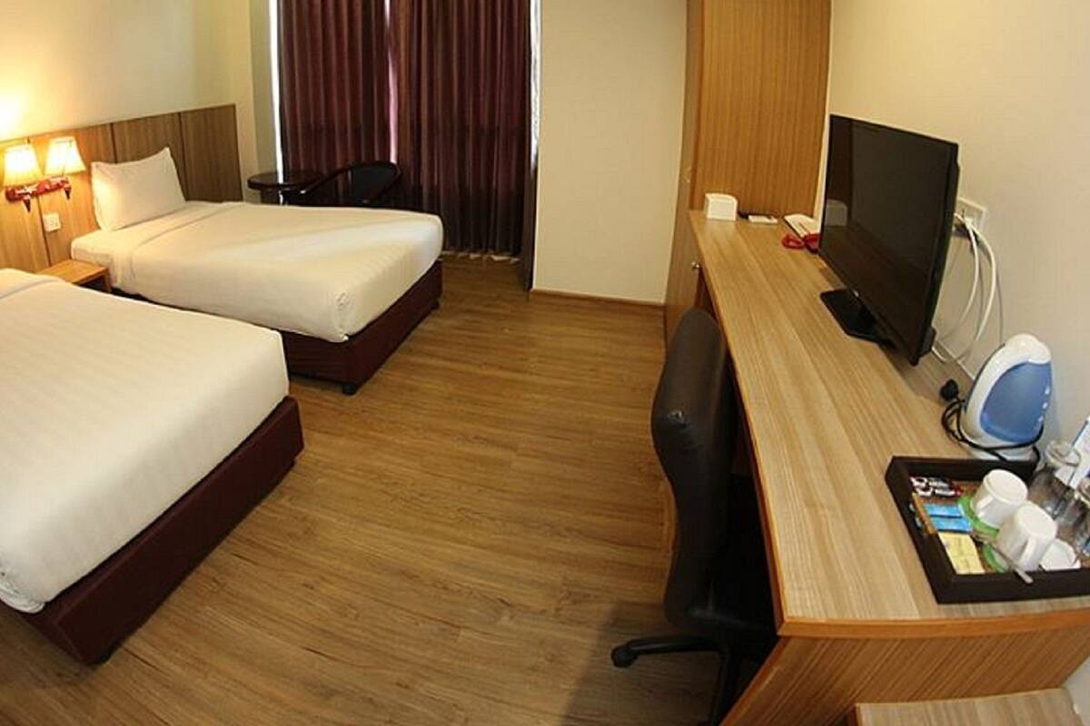 A hotel room with two beds, a desk with a computer and a coffee maker, and a chair.