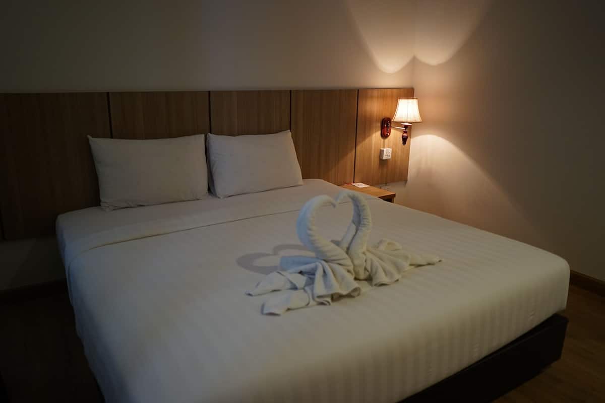 A neatly made bed with a towel arranged in a heart shape on the bed.
