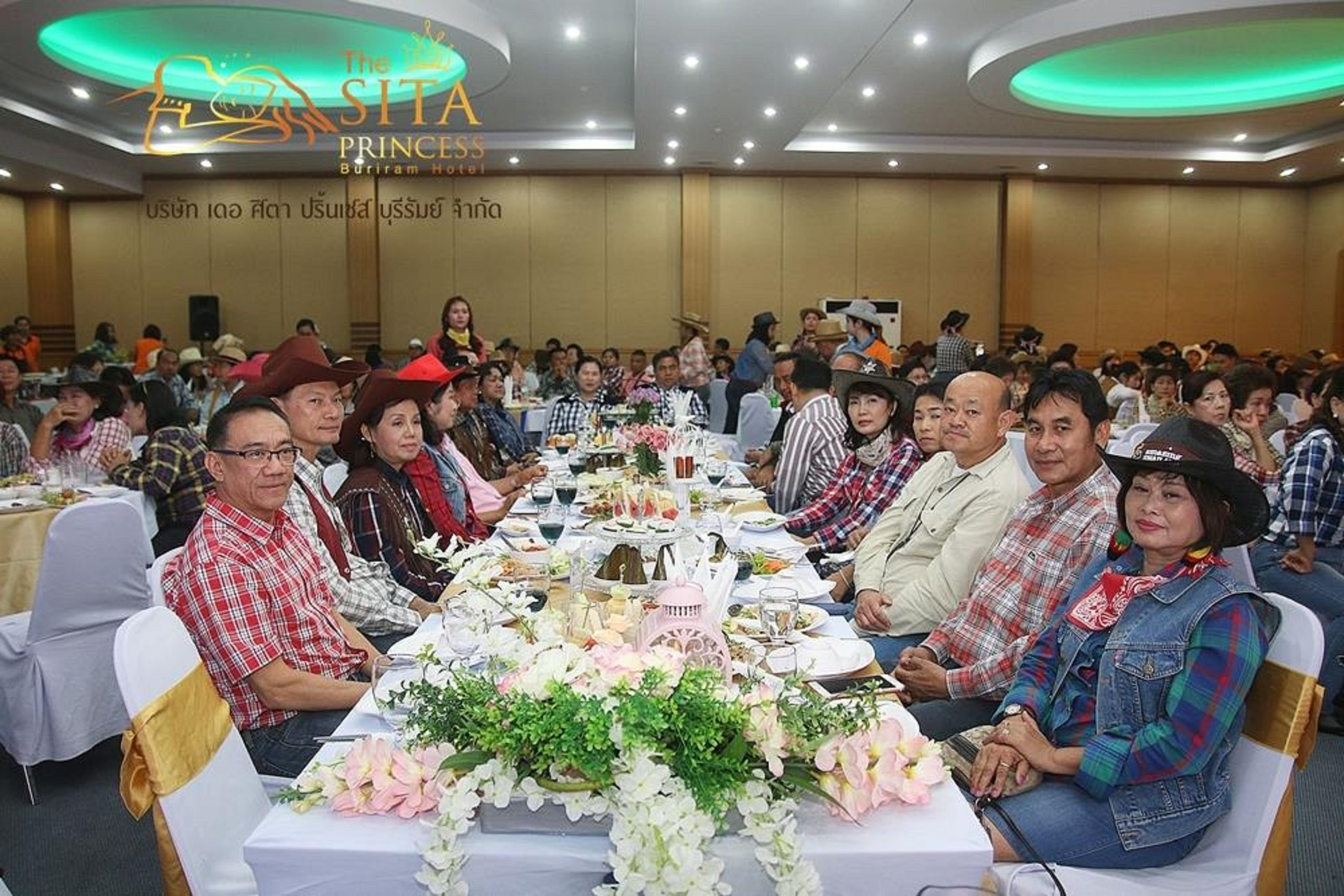 Un salón de banquetes con mesas redondas dispuestas para un evento formal, con centros de mesa florales y comensales sentados.