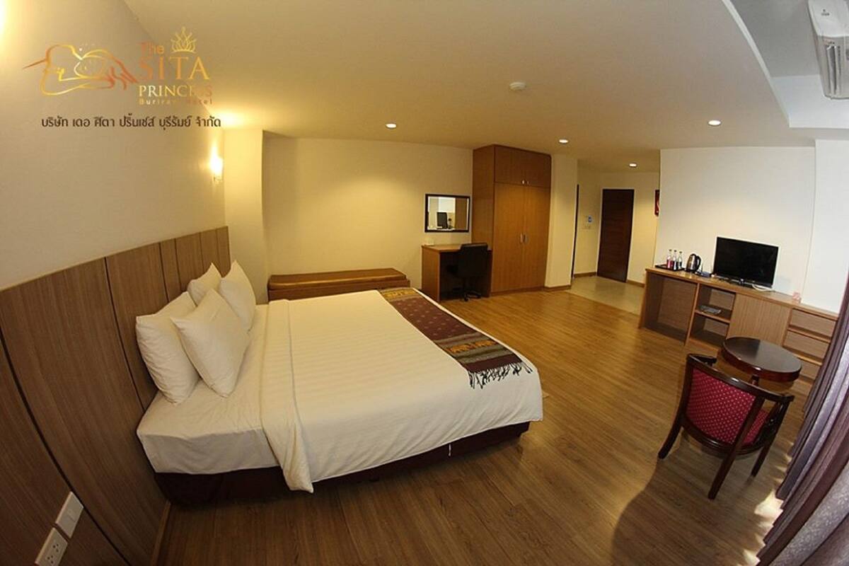 A hotel room with a large bed, a desk, a television, and a small dining area.