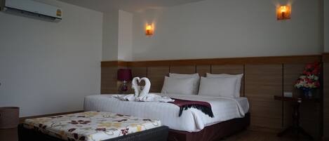 A hotel room with a large bed, a bedside table with a vase of flowers, an air conditioning unit, and a wall-mounted light fixture.