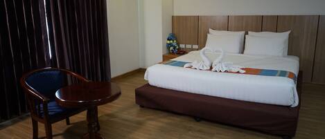 A hotel room with a wooden floor, a bed with white and brown bedding, a wooden nightstand with a vase of flowers, and a wooden chair.