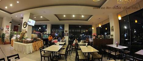 A restaurant with multiple tables and chairs, a buffet area, and a television screen.