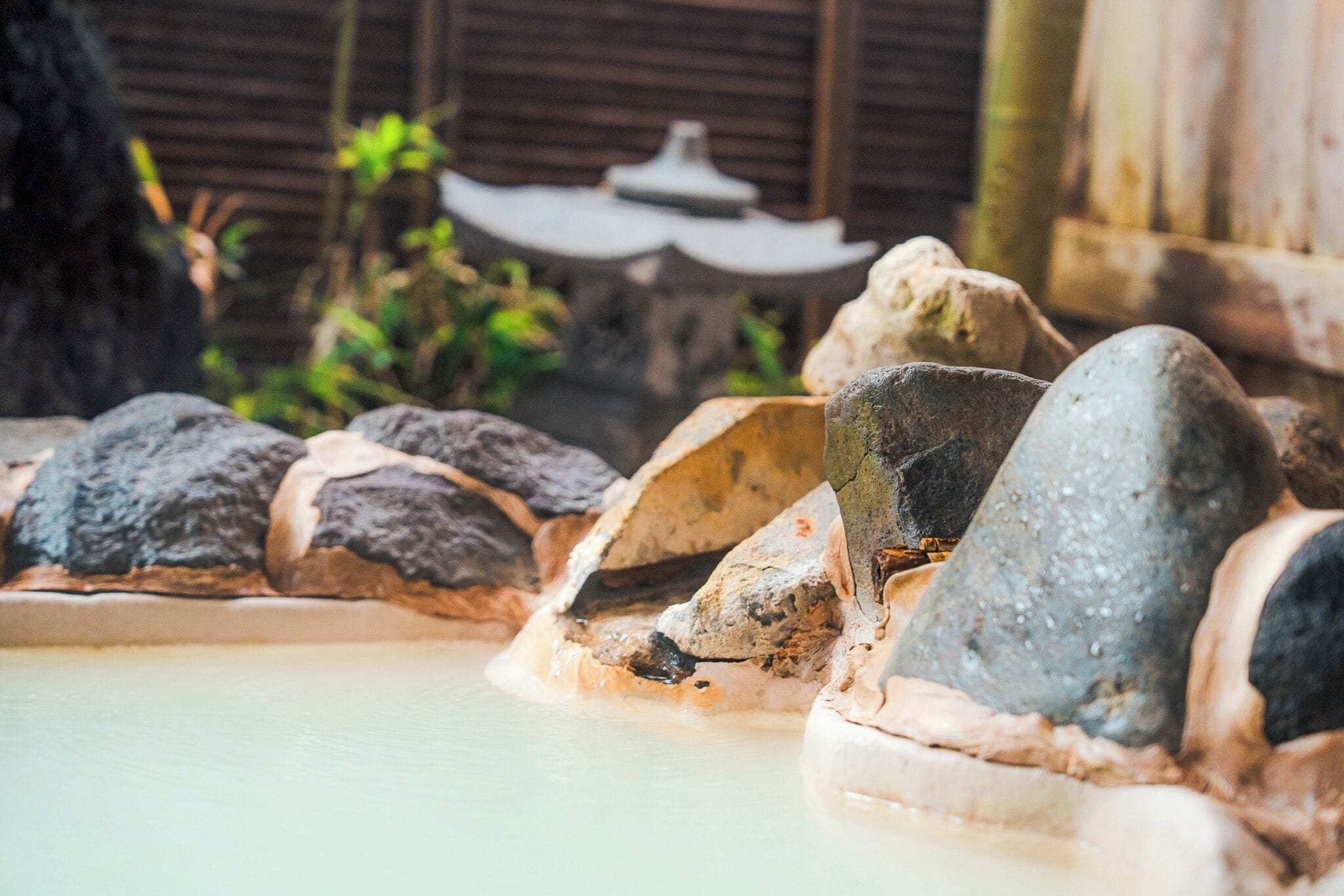 Un jardín japonés tradicional con un estanque de piedra, rocas y una estructura de madera al fondo.
