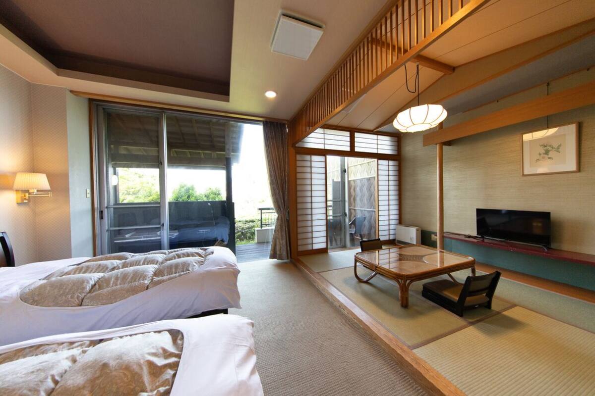 A hotel room with two beds, a TV, a sliding door to a balcony, and a traditional Japanese-style table.