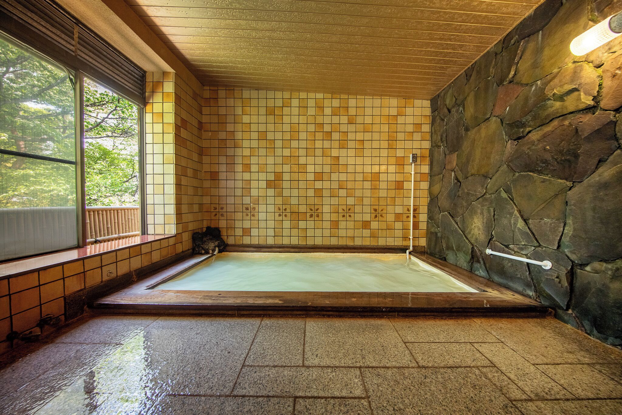 Un onsen japonés tradicional con pared de piedra, suelo de baldosas y techo de madera.