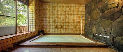Un onsen japonés tradicional con pared de piedra, suelo de baldosas y techo de madera.