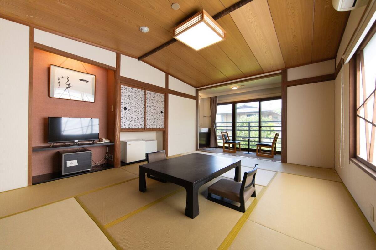 A traditional Japanese room with tatami flooring, a low table, a television, and sliding doors leading to a balcony.