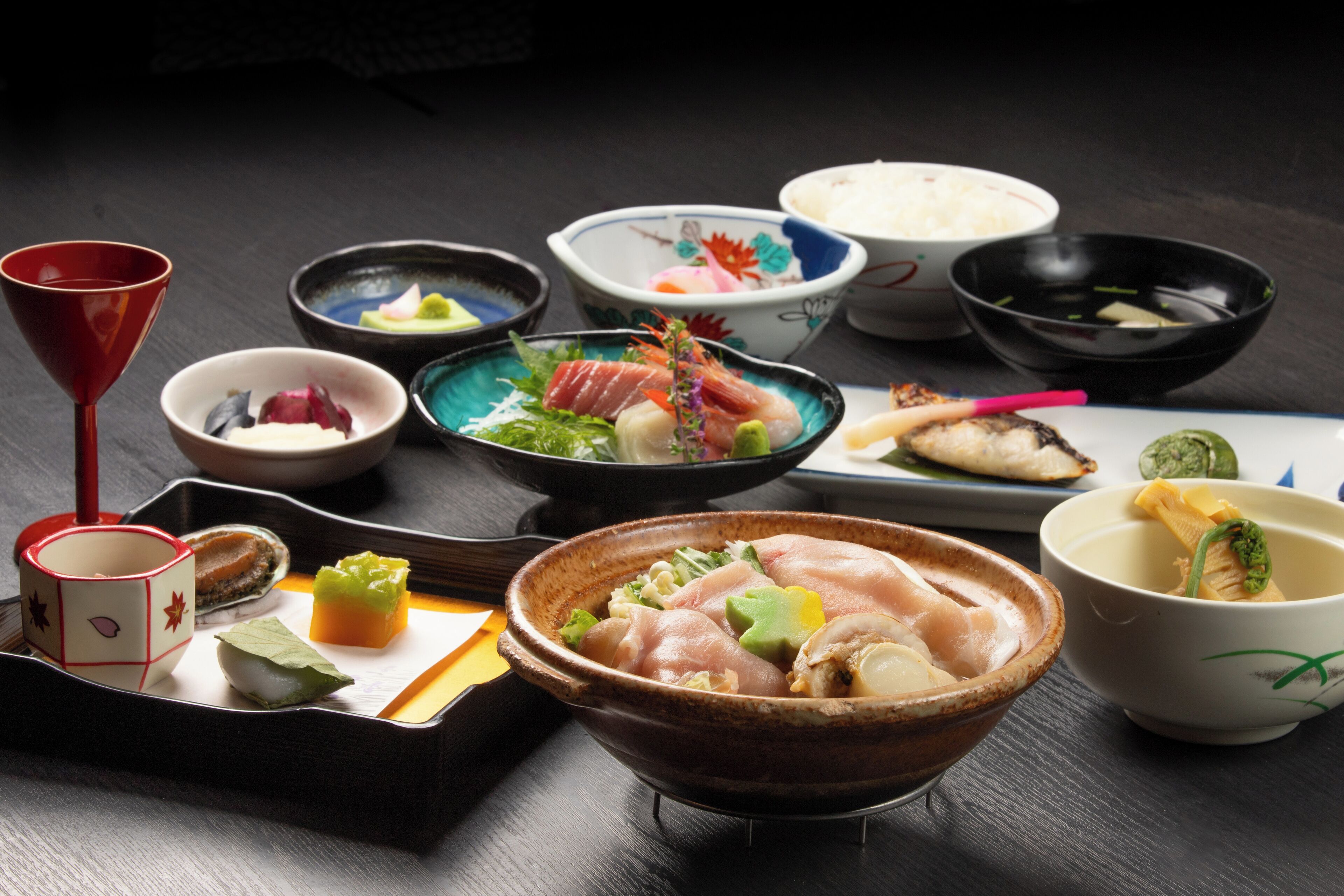 Een verscheidenheid aan traditionele Japanse gerechten, waaronder sushi, sashimi en andere lekkernijen, met kleine schaaltjes en een kopje.