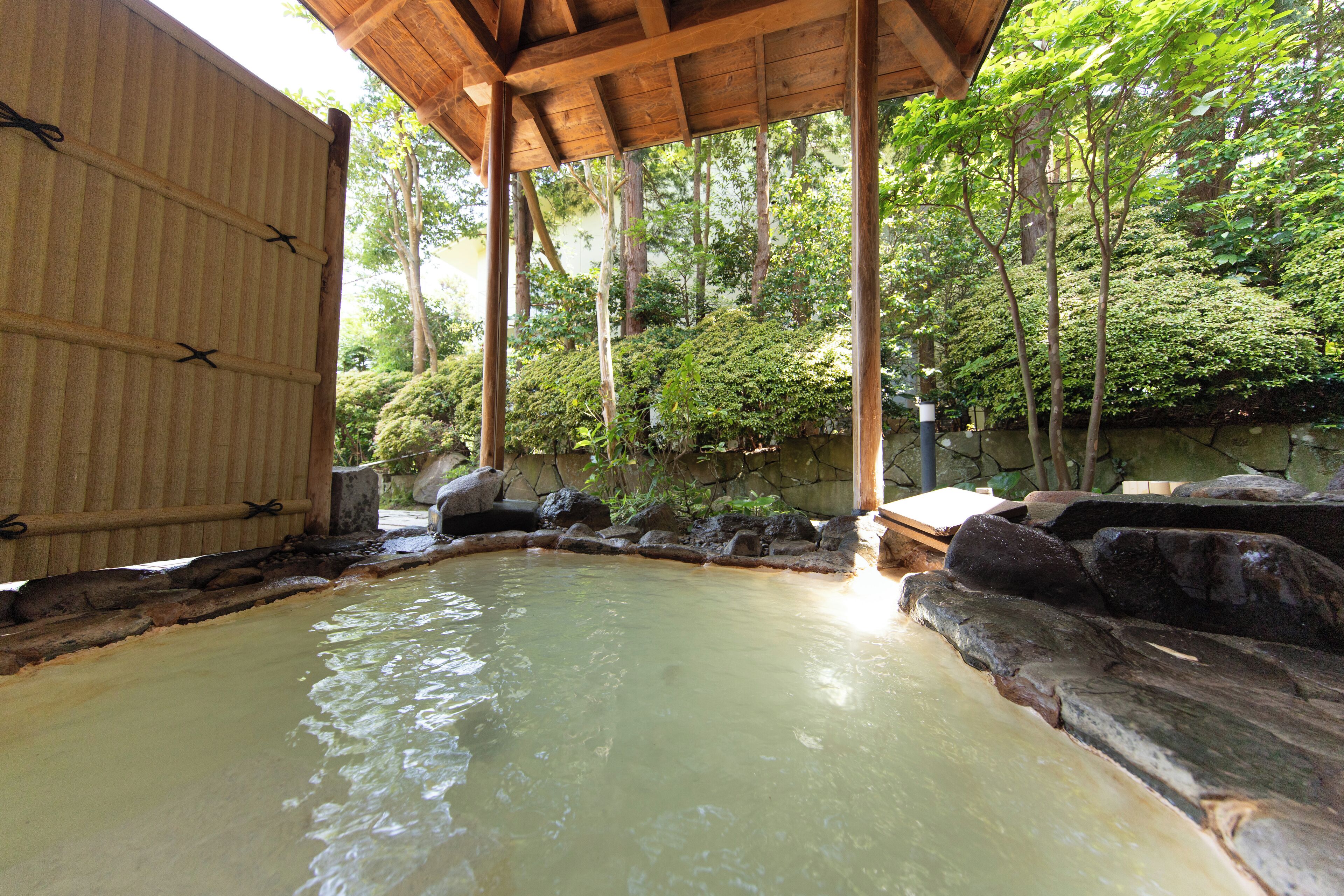 A traditional Japanese onsen with a wooden roof and stone surroundings.