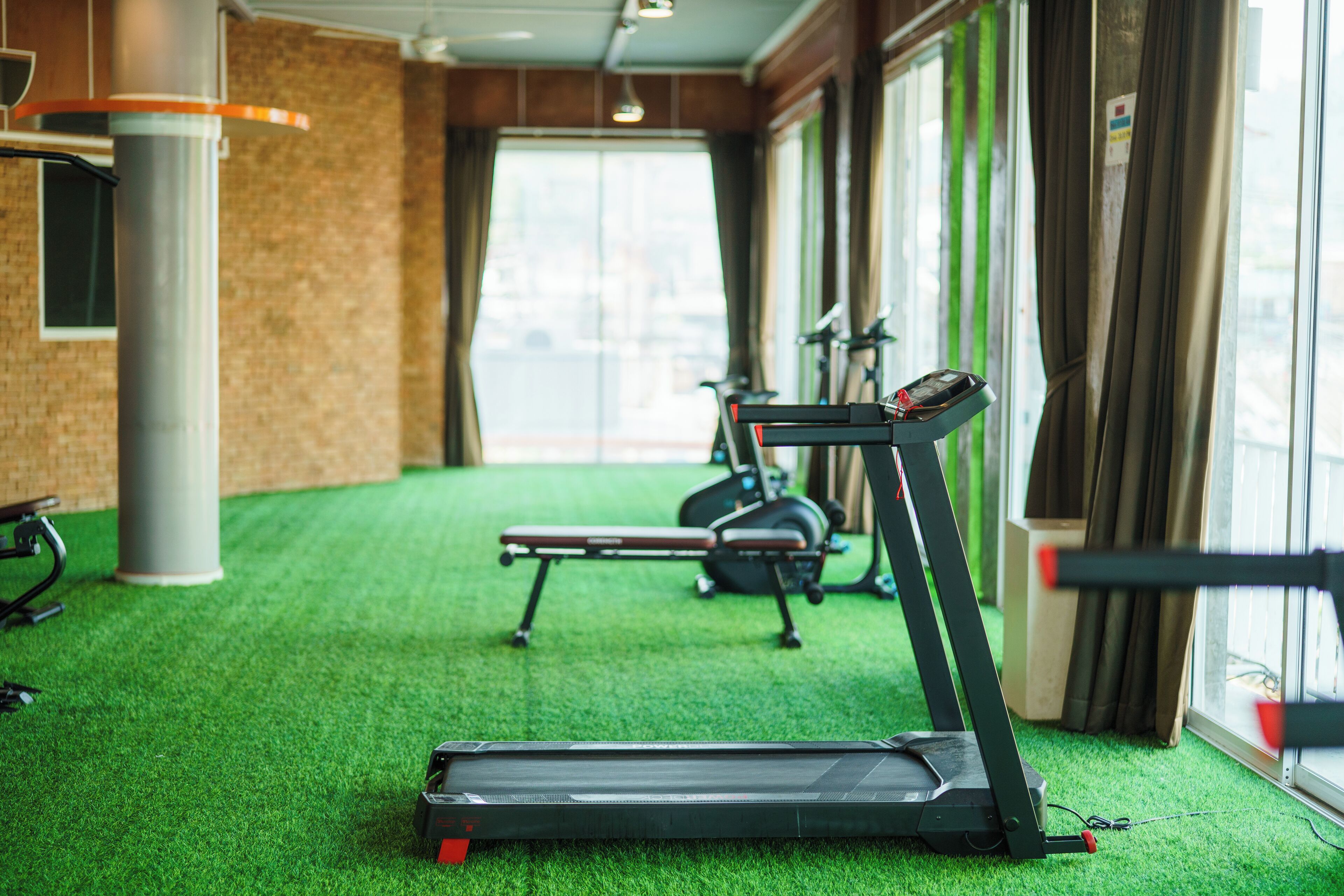 Ein Fitnessraum mit Laufbändern, Ergometer und einem grünen Teppichboden.