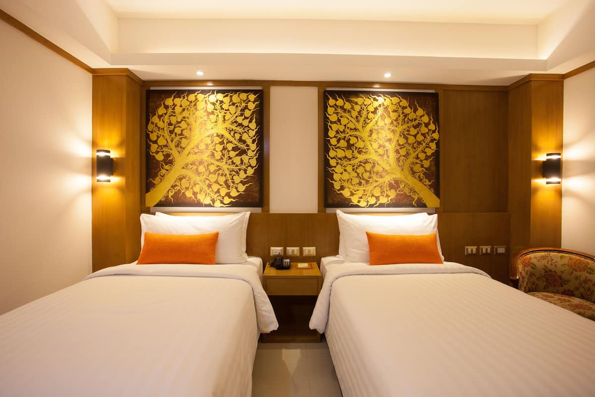 A hotel room with two beds, a nightstand, and a wall-mounted lamp.