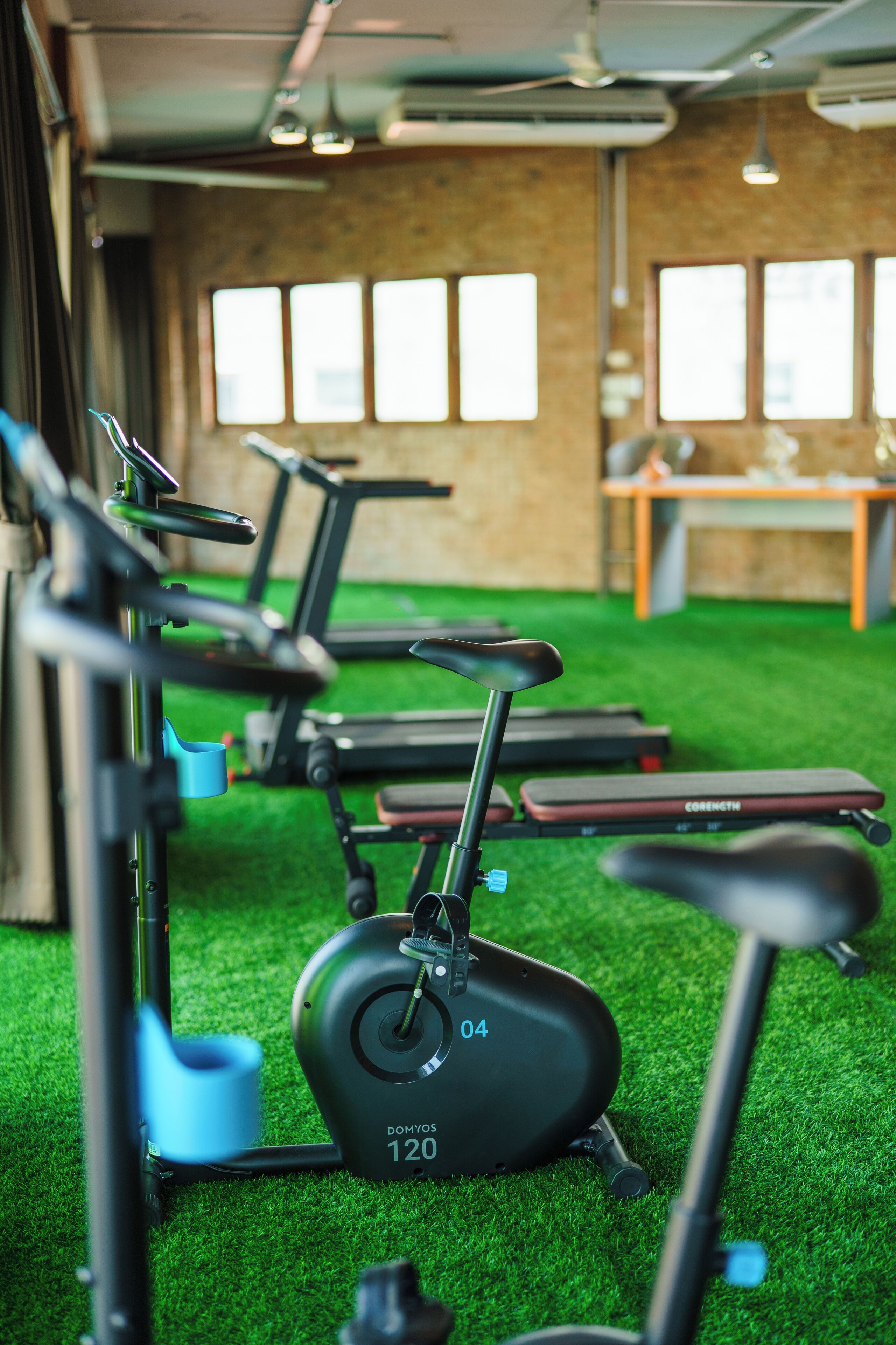 Ein Fitnessraum mit Trainingsgeräten, darunter Laufbänder und ein Crosstrainer, auf einem grünen Boden.