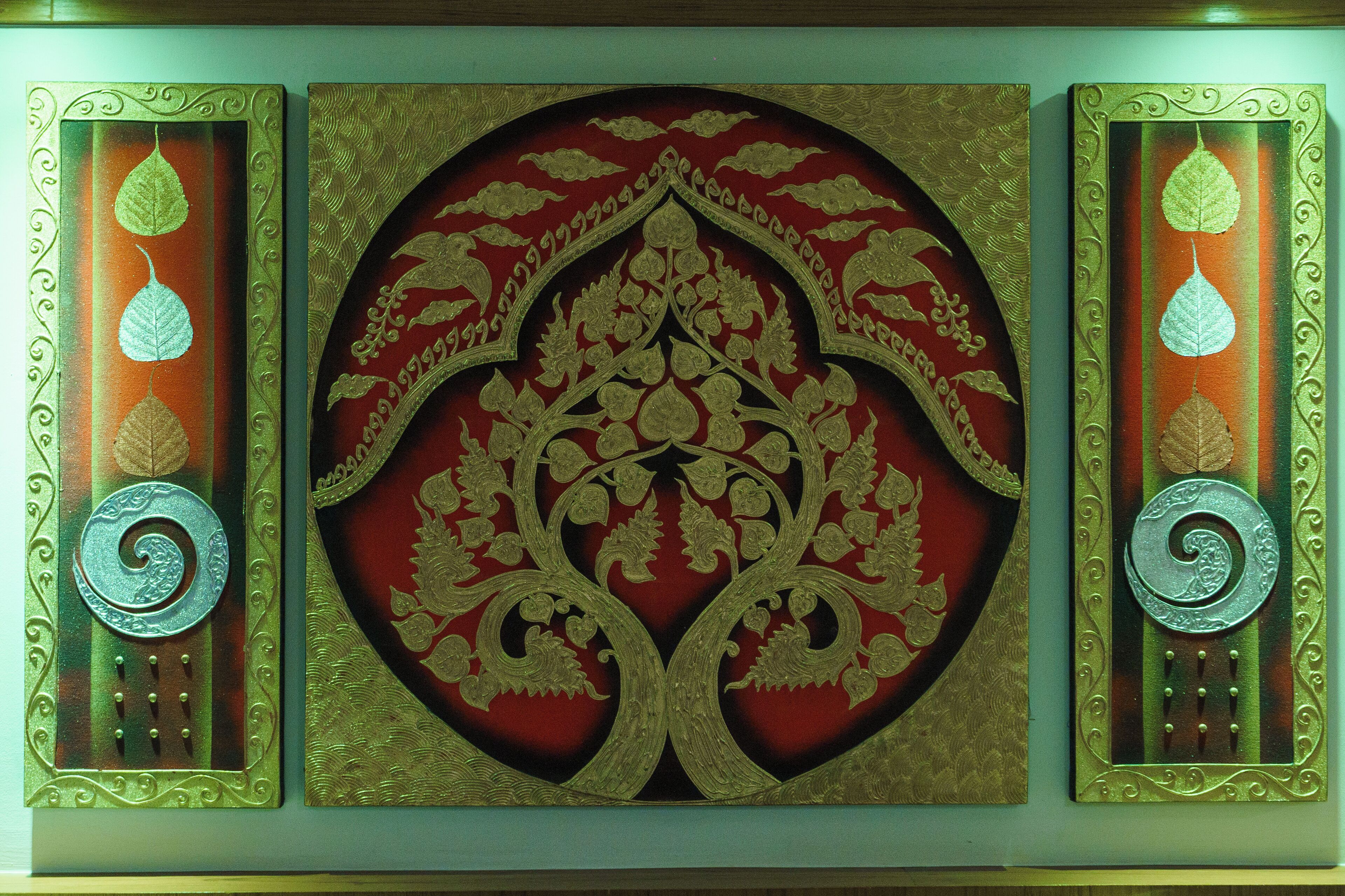 A decorative panel with intricate gold patterns and a central circular design, flanked by two vertical panels with leaf motifs.