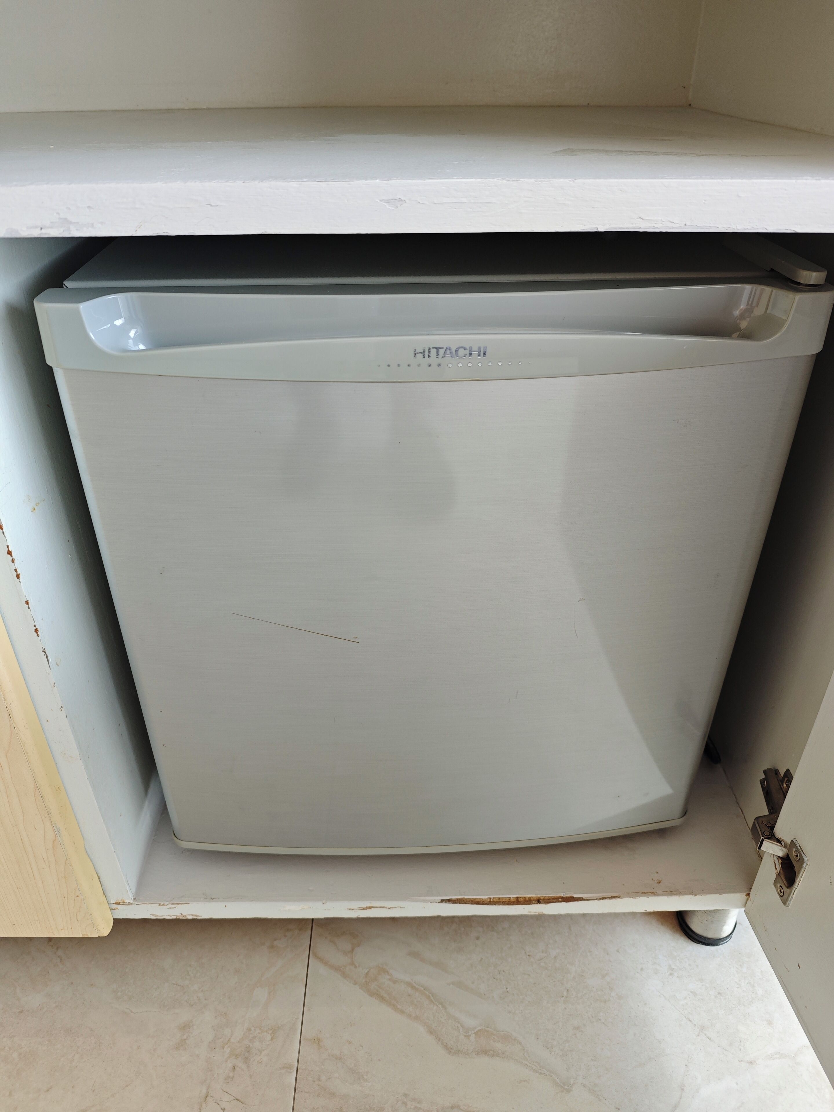 A white Hitachi refrigerator in a kitchen with a tiled floor and a wooden countertop.