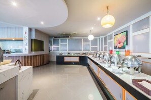 Un hall d’hôtel moderne avec un comptoir d’accueil, un espace buffet avec des points de service de restauration et un grand tableau accroché au mur.