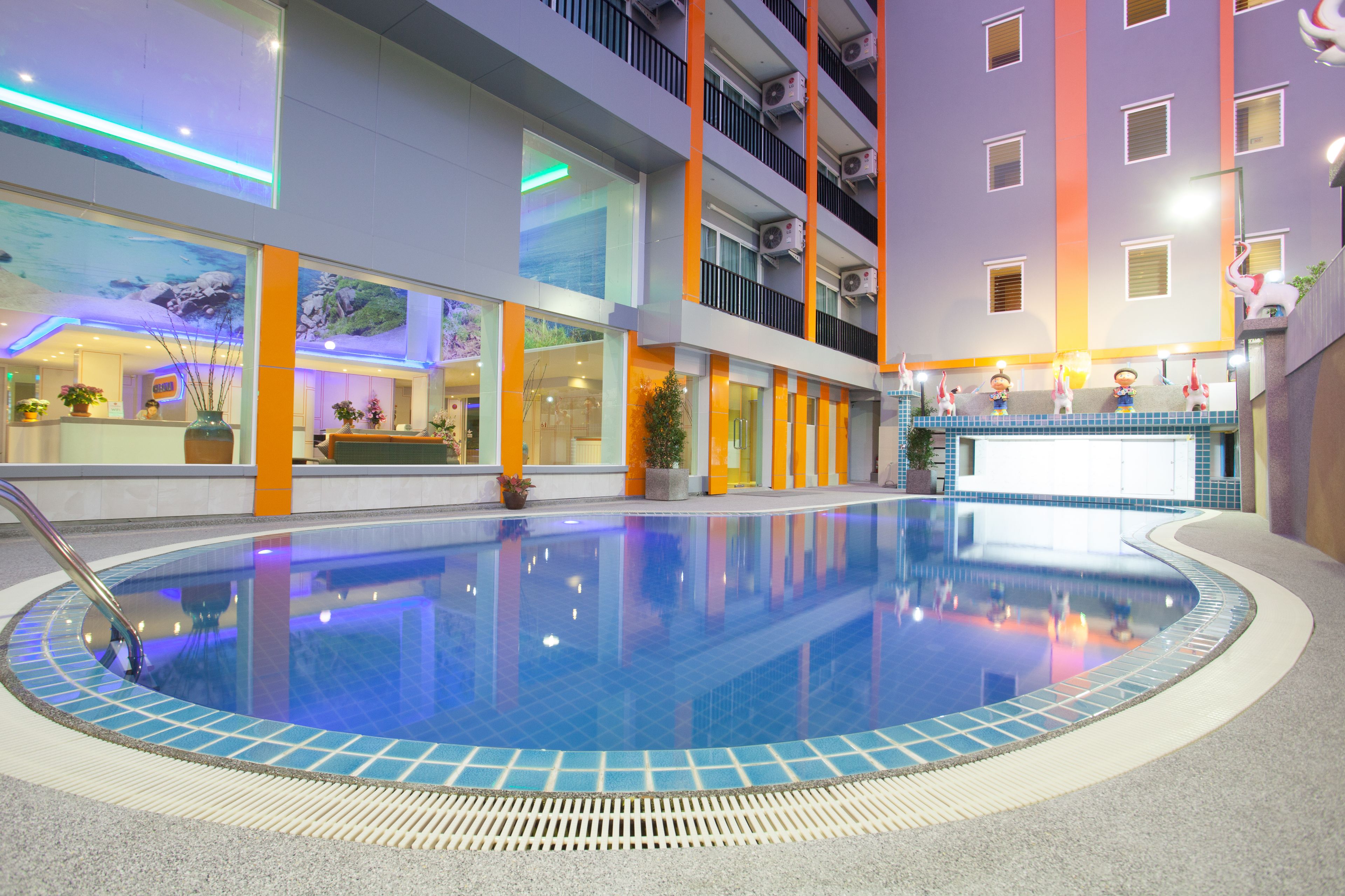 An indoor swimming pool with a tiled edge, surrounded by a reception area with a counter and potted plants.