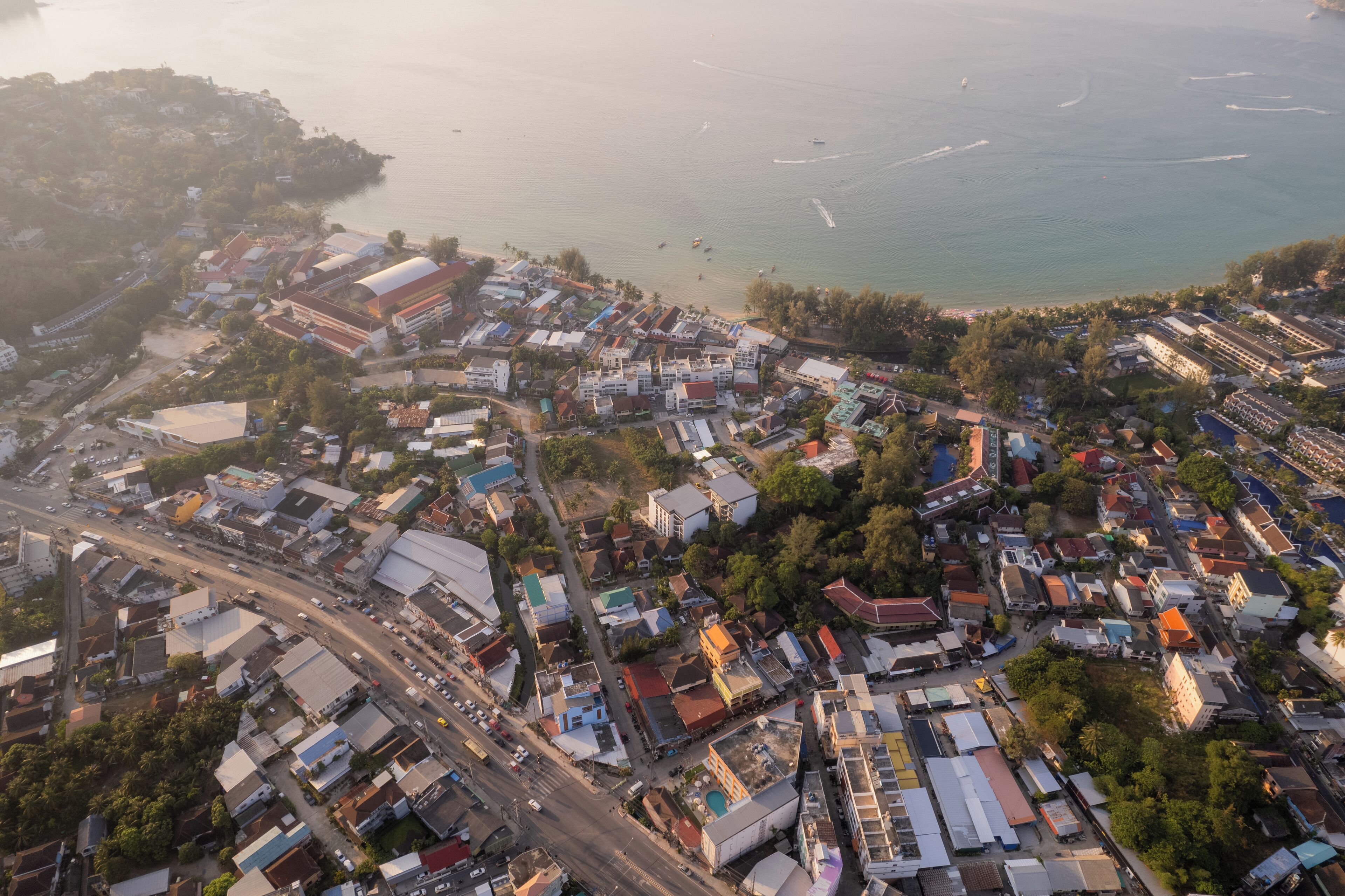 An aerial view of a coastal town with a mix of residential and commercial buildings, a main road, and a beach in the background.