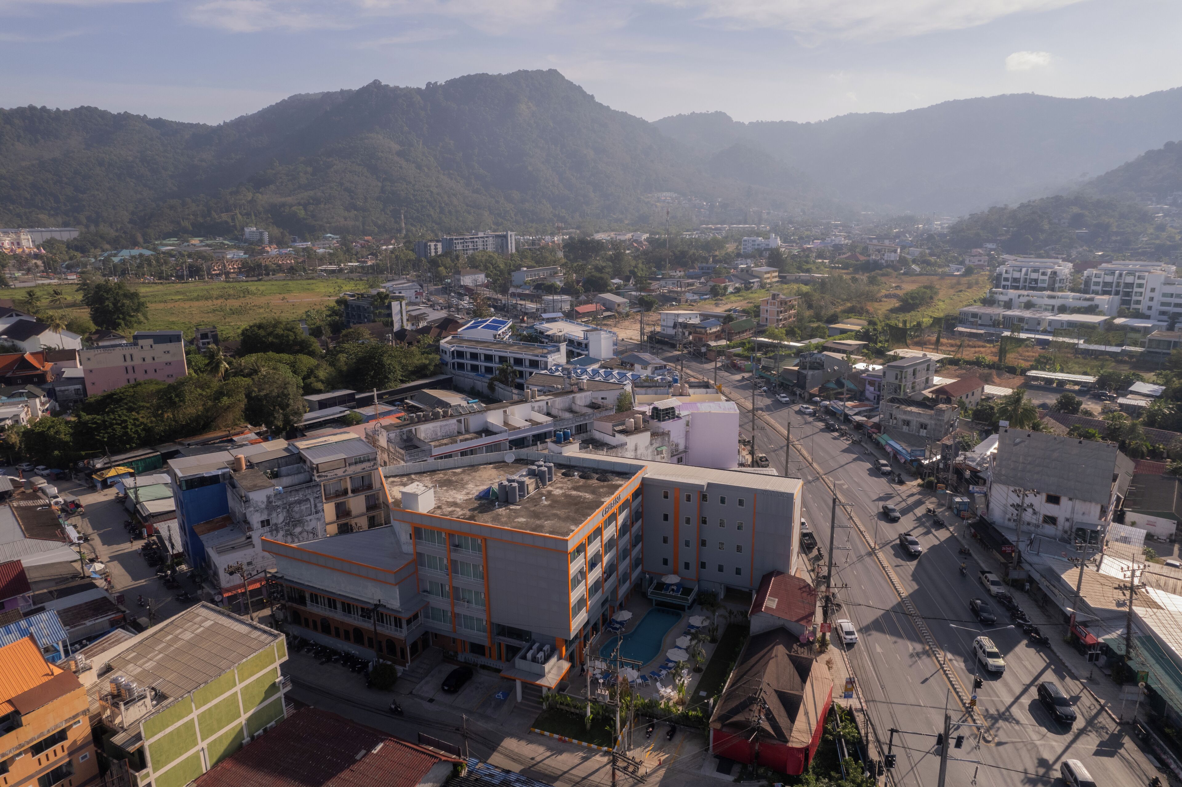 A cityscape with a mix of modern and older buildings, a central road, and surrounding hills.