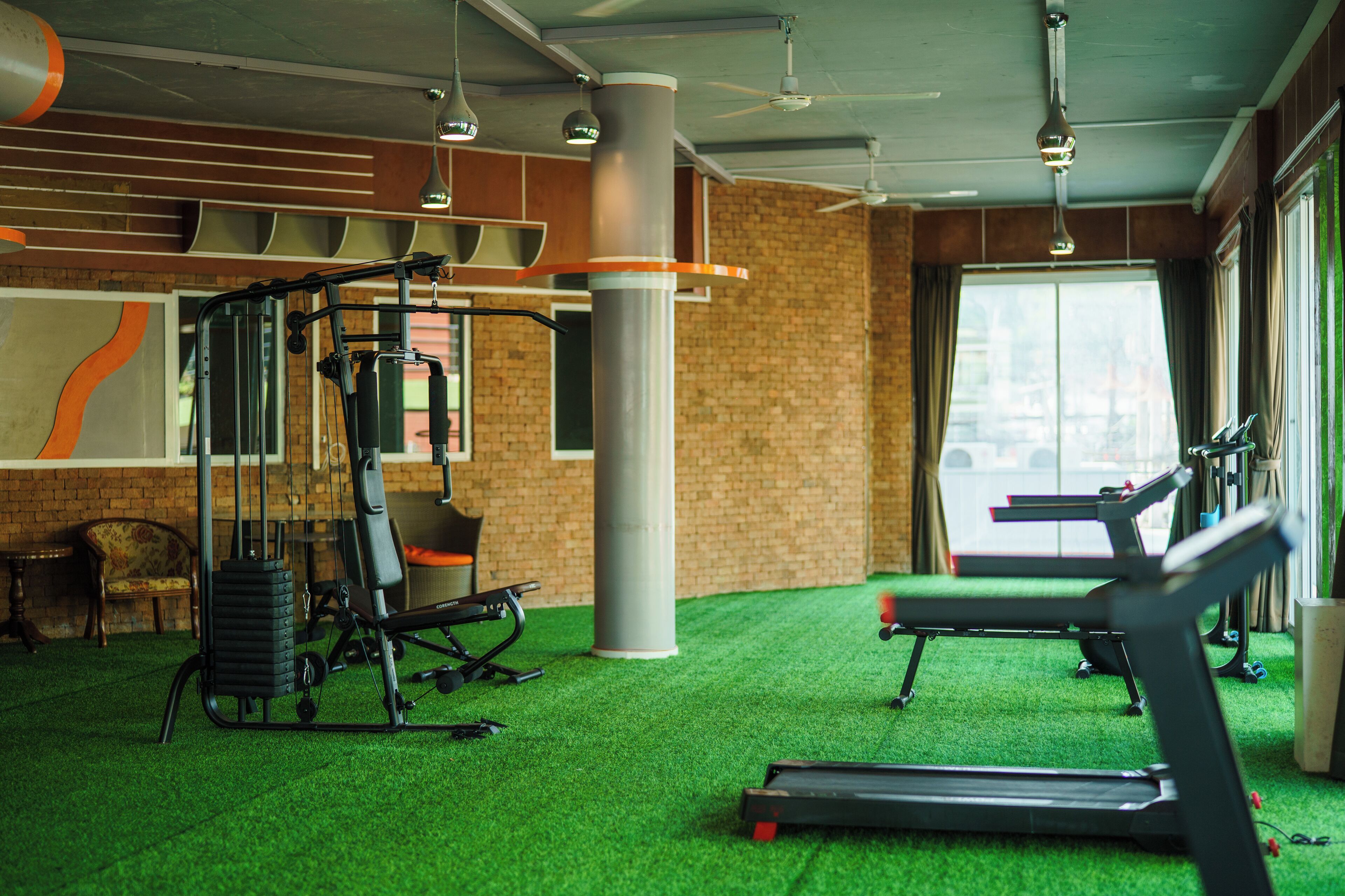 A gym with exercise equipment, a green artificial turf floor, and large windows.