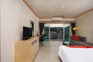 Une chambre d’hôtel comprenant un lit, un bureau avec une télévision, un canapé, un fauteuil et un balcon offrant une vue sur la ville.