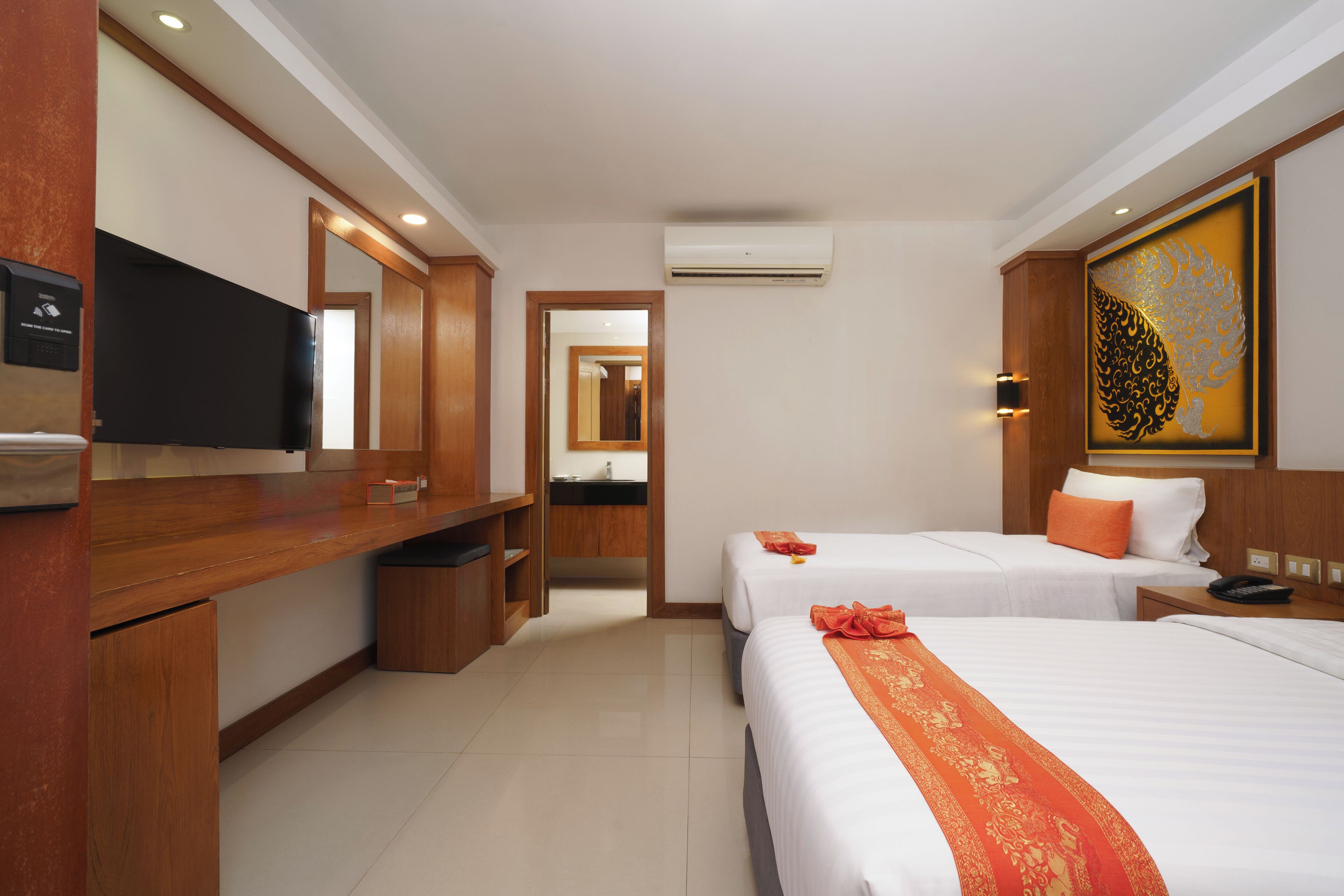 A hotel room with two beds, a desk, a television, and a bathroom visible through an open door.