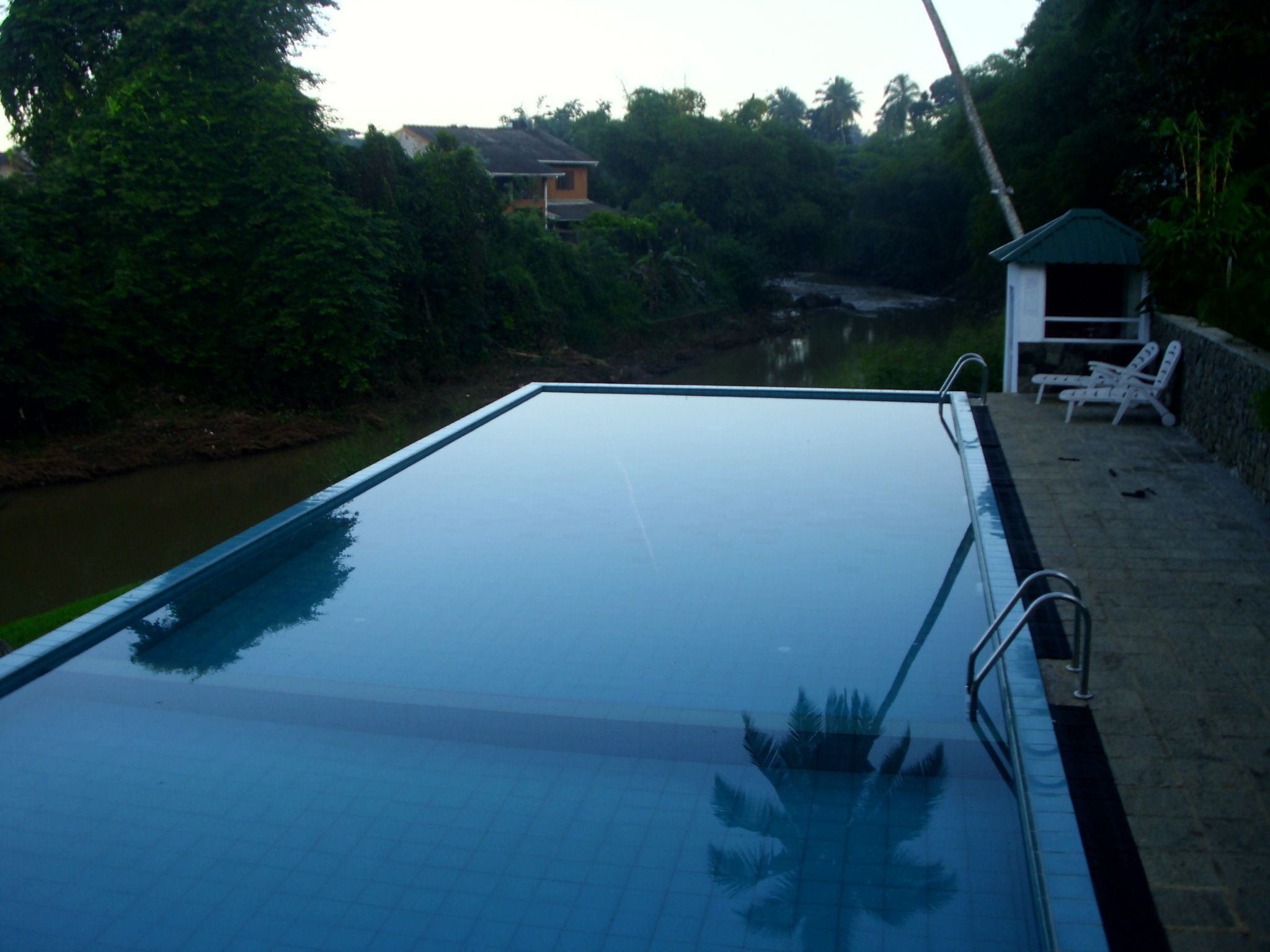 An outdoor swimming pool with a clear view of the surrounding greenery and a small structure with lounge chairs.