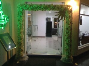 Entrada de hotel con puerta de vidrio, un marco decorativo verde y un pequeño cartel a la izquierda.