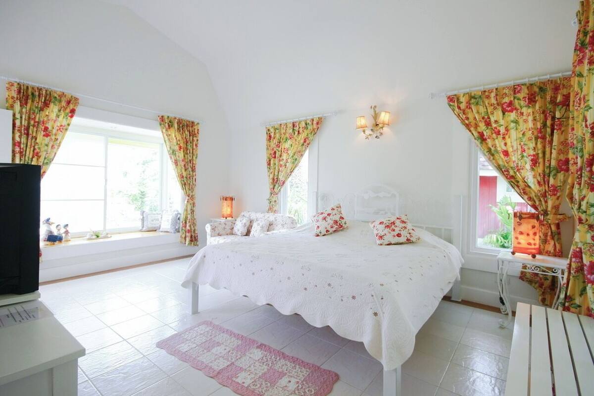 A bedroom with a bed, curtains, a nightstand, a lamp, and a window.