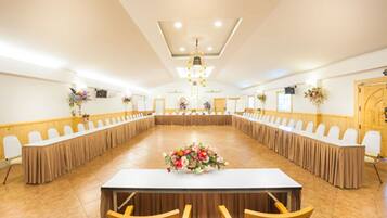 Un salón de conferencias con una larga mesa, sillas y centros de mesa con flores.