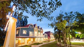 A row of multi-story buildings with a well-maintained lawn and a white fence. - Belmont Village (Pak Chong)