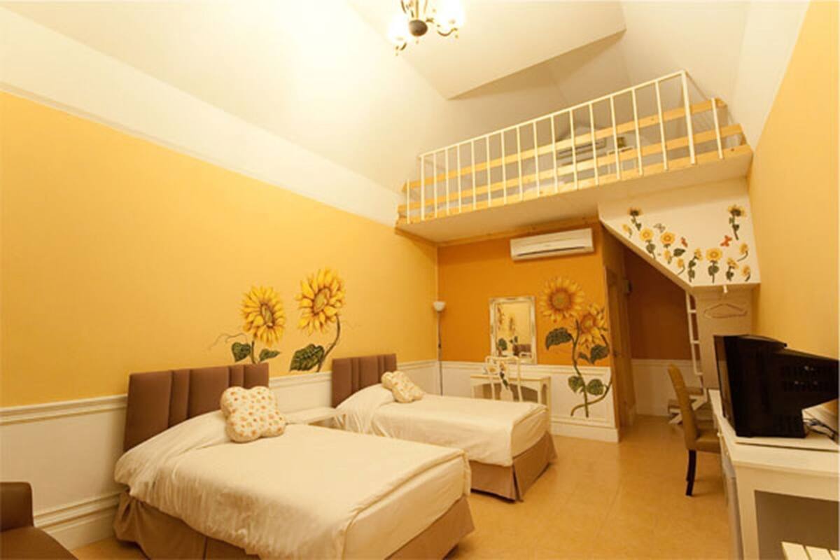 A bedroom with two beds, a desk, a chair, a staircase, and a sun decoration on the wall.