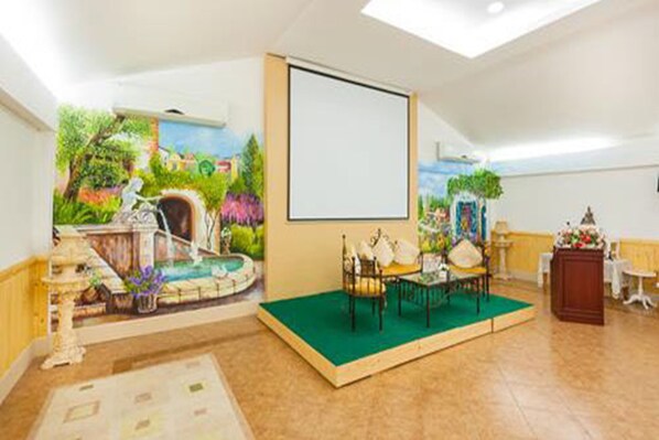 Un salón de conferencias con una pantalla grande, alfombra verde y un mural con una fuente.