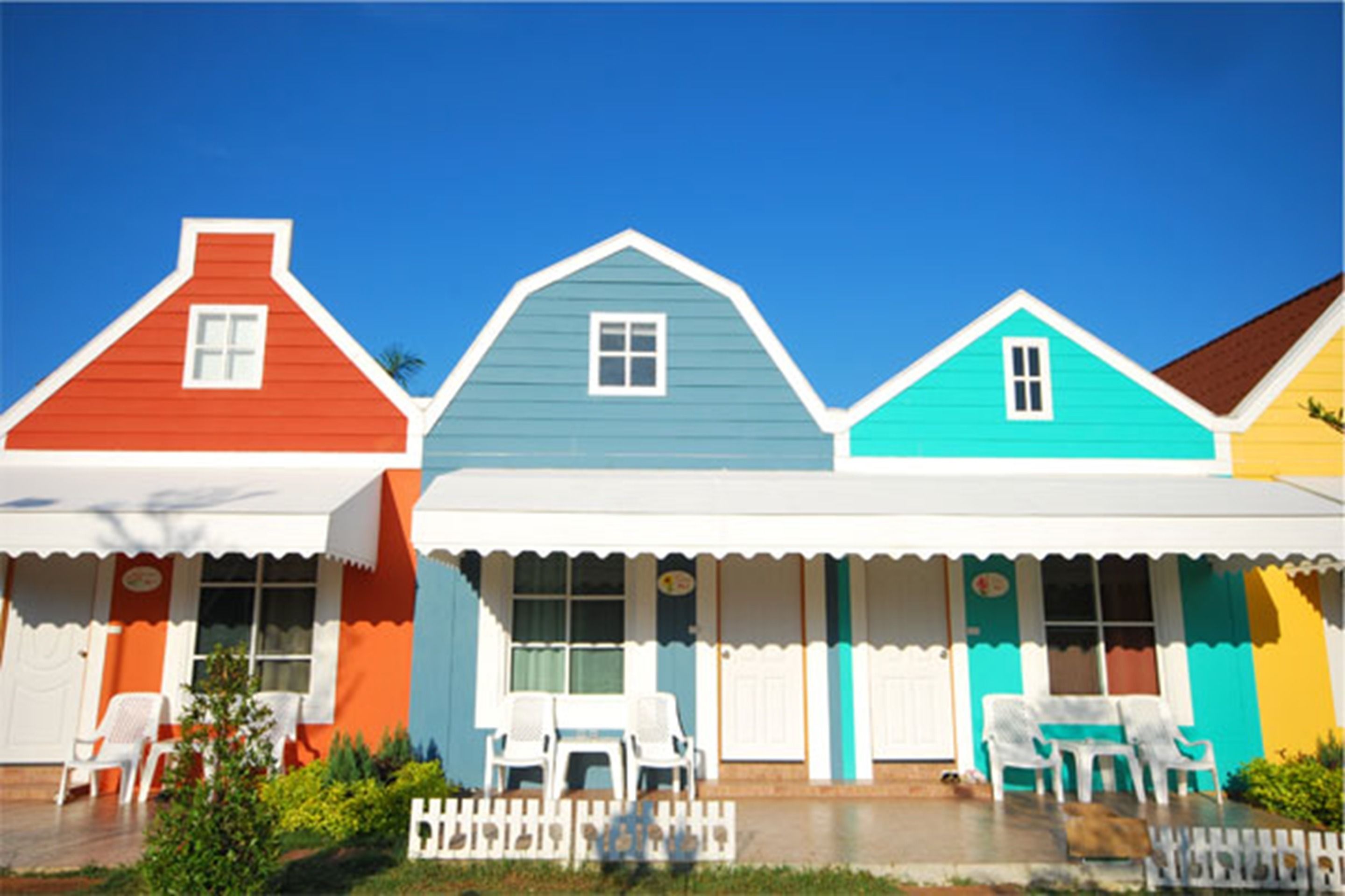 A row of colorful houses with white picket fences and white chairs outside.