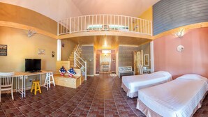 A room with two beds, a desk, a TV, and a staircase leading to a balcony. - Belmont Village (Pak Chong)