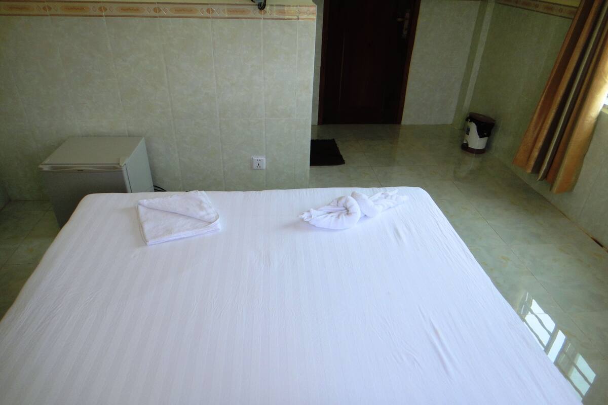A hotel room with a large bed, a small bedside table, and a door leading to another room.