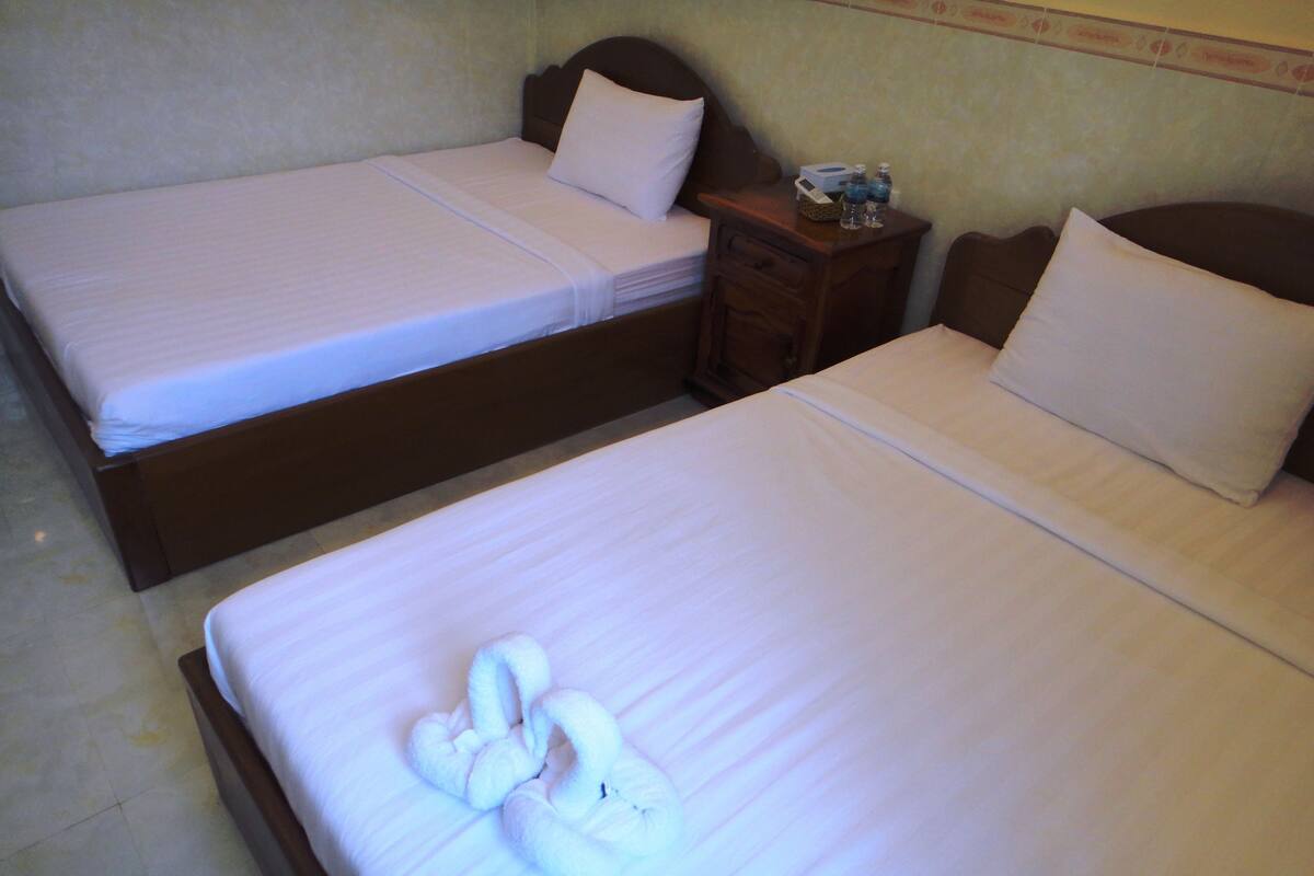 Two twin beds with white linens, a wooden headboard, and a nightstand with a lamp and a bottle.