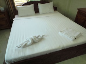 A neatly made bed with white linens, a folded towel, and a neatly folded blanket on a wooden headboard. - Borey Vatanac Guesthouse (Kampot)