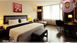 A Deluxe D Double Room with a large bed, bedside tables, a desk, a chair, and a bench. - Sunee Grand Hotel (Ubon Ratchathani)