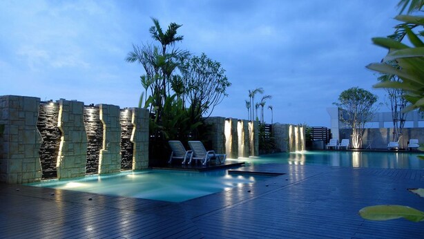 A pool area with lounge chairs and a stone wall with water features.