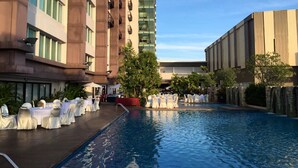 A hotel pool area with tables and chairs set up for an event, surrounded by buildings with balconies and a clear sky.